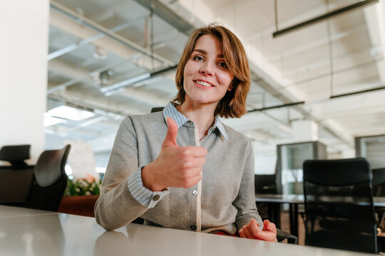 Businesswoman showing thumbs up and smiling in modern office