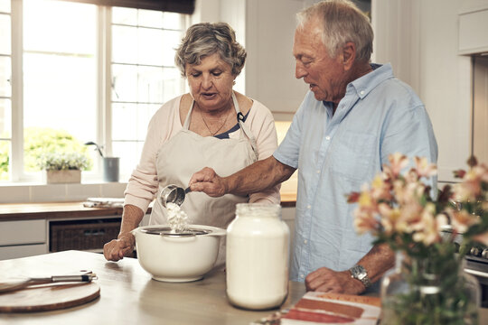 Support, old couple and baking with flour in home for cake recipe, retirement hobby and bonding. Senior people, cooking assistance and sieve in kitchen for dessert preparation, help and relationship