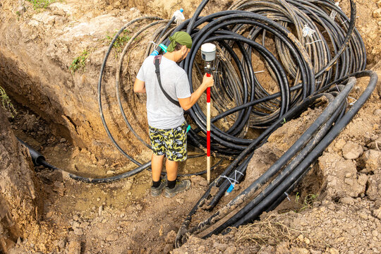 Surveyor checking cable location compliance with design position using GNSS receiver at construction site trench