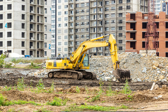 Crawler excavator performing vertical planning and site preparation work near crushed stone pile at residential construction zone