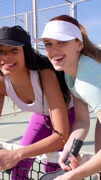 Two female pickleball players posing and smiling at the net