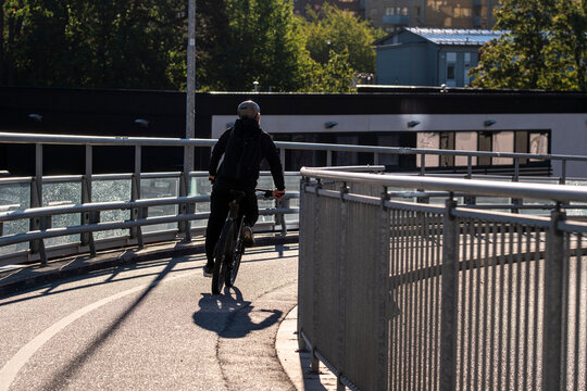 Cyclist on bicycle crossing bridge in Stockholm Sweden along urban pathway by railing with sunlight and shadow creating graphic travel scene