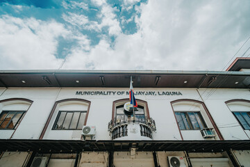 Majayjay Municipal Hall Building Facade in Laguna, Local Government Office with Philippine Flag and Town Sign under Cloudy Blue Sky, Philippines Provincial Architecture © Gids Stories