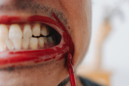 Macro shot of Thai man pulling red lipstick off teeth with fingers in intense emotional expression