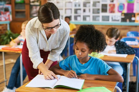 Education, teacher and help child in classroom for academic support, development and instructions. Book, educator and girl at elementary school for lesson assistance, knowledge or assessment feedback