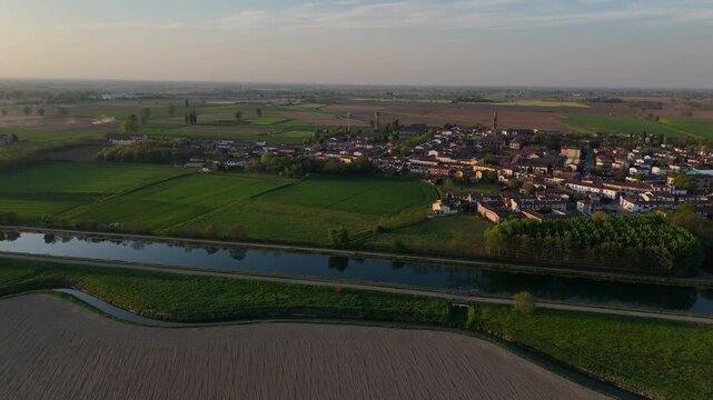 Spinadesco Cremona Lombardy Italy with Canale Milano Cremona Po navigation canal in foreground and village beyond across Pianura Padana farmland under sunset light, drone anticlockwise orbit shot