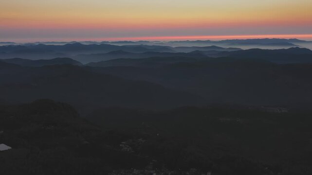 Yercaud's mountain ridges emerge from morning mist as dawn light illuminates layered peaks in Tamil Nadu, India. Slow wide angle drone shot captures the expansive valley view at sunrise.