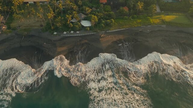 Drone captures rip currents and wave patterns on a tropical black sand beach at sunrise, glowing in warm golden light with dynamic ocean textures and flowing coastal motion.