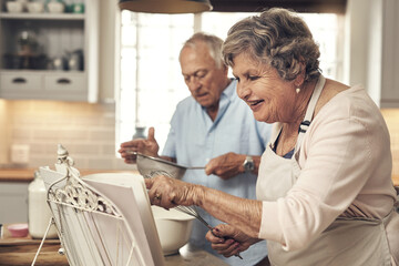 Obraz premium Baking, reading and book with old couple in kitchen of home for love, bonding and cookies recipe. Ingredient list, support and cooking with senior man and woman in apartment for meal and food
