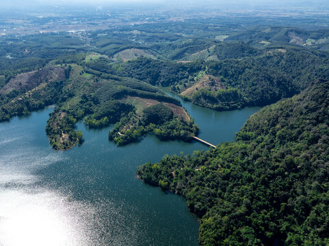 Sunlight Reflects Off A Winding Mountain Reservoir Surrounded By Lush Green Forests And Rolling Hills