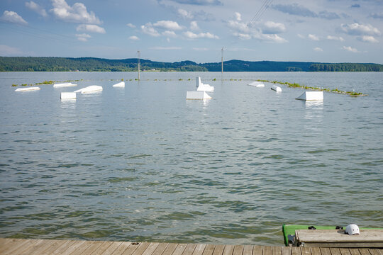 Empty wakeboard park on a calm lake with white obstacles and ramps under a cloudy sky