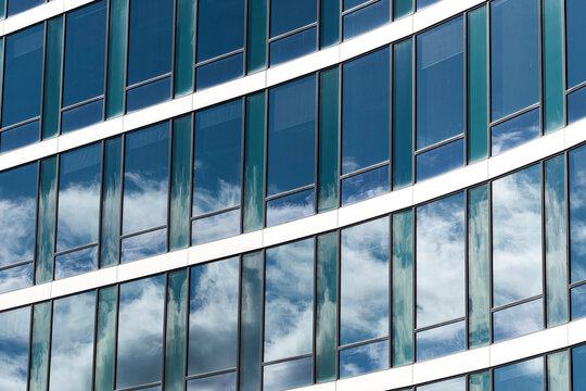 Cloud reflections on modern architecture facade building glass reflection windows forming abstract pattern geometry with sweeping curves clean lines and sky