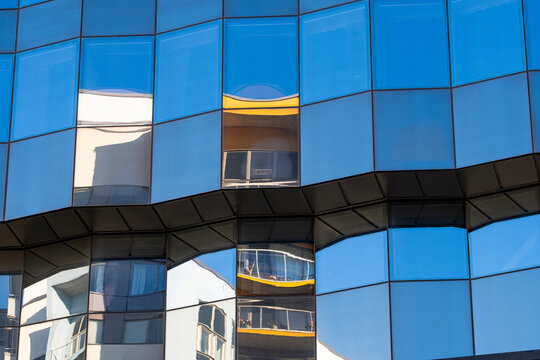 Curved modern architecture facade building glass reflection windows producing abstract pattern geometry with wavy distortion and smooth mirrored blue panels