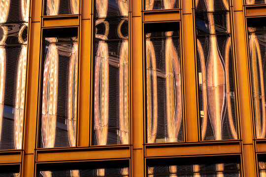 Warm metallic frames on modern architecture facade building glass reflection windows creating abstract pattern geometry with amber tones repetition and shine