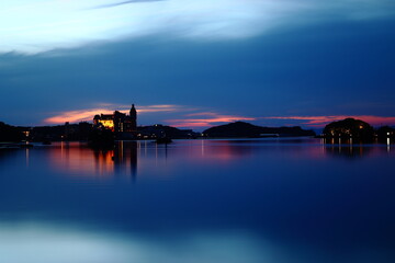 Naklejka premium Twilight lake reflection with illuminated waterfront building and peaceful blue hour sky