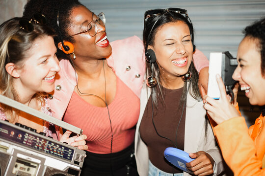 Group of multiracial girls having fun together dancing listening music while taking photo with a vintage instant camera outdoor - Party, nightlife and people lifestyle concept 