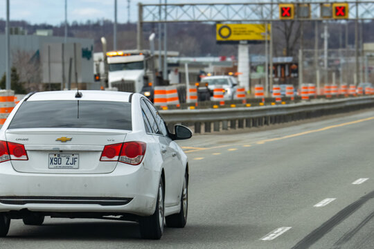 Quebec, Canada, 24 April 2026 : White Chevrolet Cruze sedan drives on a highway approaching a toll plaza with traffic cones.