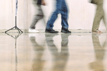 Obraz premium Blurred people walking indoors with floor reflections, dynamic motion and urban lifestyle scene, minimal background, candid perspective