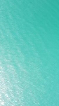 Vertical aerial view over calm azure sea water surface. Sun glare. Abstract nautical summer ocean nature. Holiday, vacation and travel concept. Nobody. Weather and climate change
