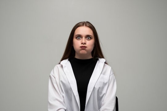 Young woman puffing cheeks and widening eyes, creating a funny face, showing humorous and playful expression