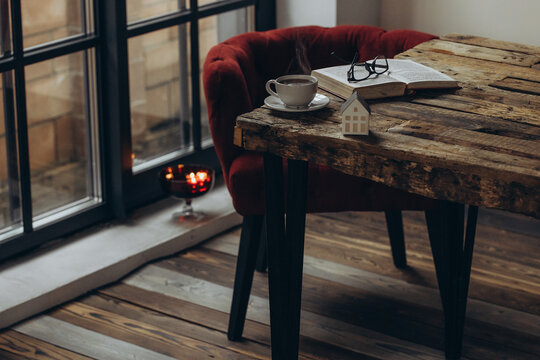 Home decor and comfort. A book, glasses, and a cup of tea on a wooden table. A sitting area in a cozy room. 