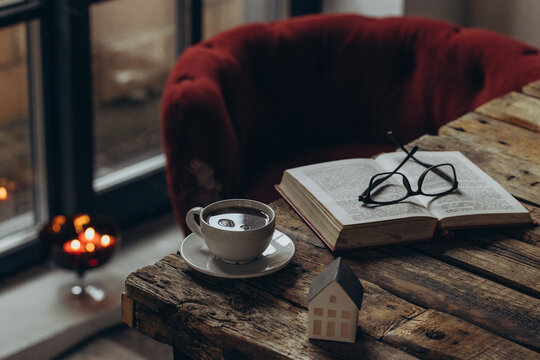 Home decor and comfort. A book, glasses, and a cup of tea on a wooden table. A sitting area in a cozy room. 