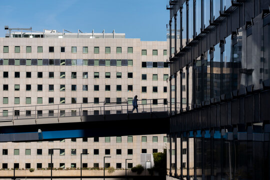 Pedestrian silhouette crosses modern Defense bridge in Paris business district where urban skyscrapers rise above a bright corporate commute