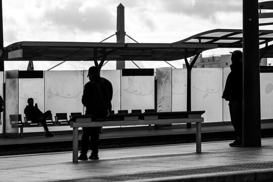 Paris commuters become silhouettes at tram station platform waiting as shadows deepen in monochrome urban transit scene during evening rush