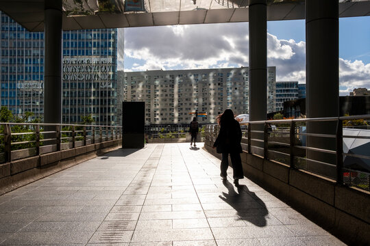 Commuting people move along Defense walkway in Paris business district as modern architecture guides the flow and shadows stretch at dusk