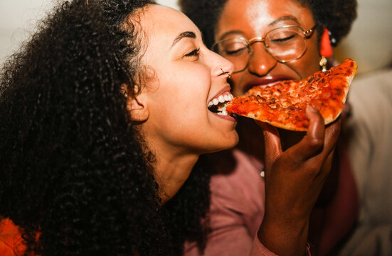 Hungry african american girls eating pizza outdoor in the streets after party concert - Food, people lifestyle  and nightlife concept - Main focus on left woman mouth - UGC flash content