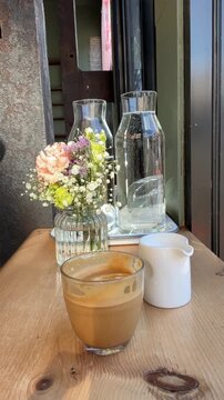 Cup of coffee, glass vases with spring flowers on a wooden table in a cozy cafe.