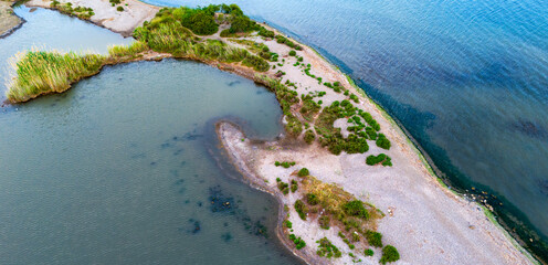 Aerial view of a curved coastal sandbar covered with vegetation meeting deep blue water © Buğra Kaan Ersoy