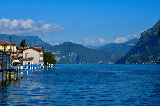 Blick vom Wasser auf die blau-wei&szlig;en Anlegepf&auml;hle und Uferh&auml;user in Carzano auf der Monte Isola, Iseosee