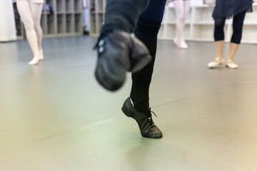 Dance class in a studio, close-up on a dancer's feet in black jazz shoes in motion, with ballet dancers wearing pointe shoes in the background.  © Schilo