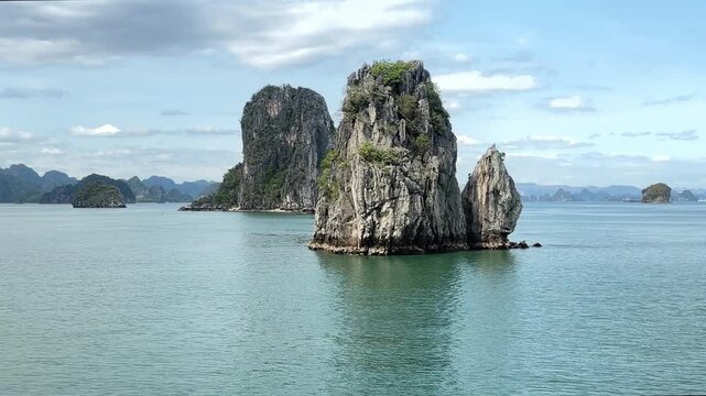 Limestone karst pillars rising from calm emerald waters of Halong Bay Vietnam, tranquil tropical seascape, serene travel destination and natural landmark