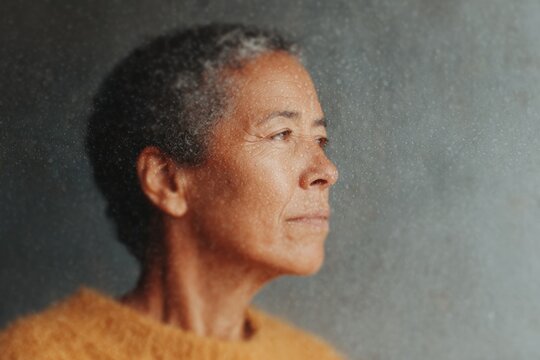 A woman in an orange sweater standing in front of a wall. she has a warm and inviting expression on her face and her hair is pulled back in a neat bun.