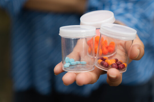 Close-up of a hand holding several small transparent containers filled with different types of pills and capsules. Concept of medication variety