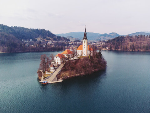 Aerial view of the Pilgrimage Church of the Assumption of Mary on Bled Island surrounded by calm lake waters and forested hills in Bled, Radovljica, Slovenia.