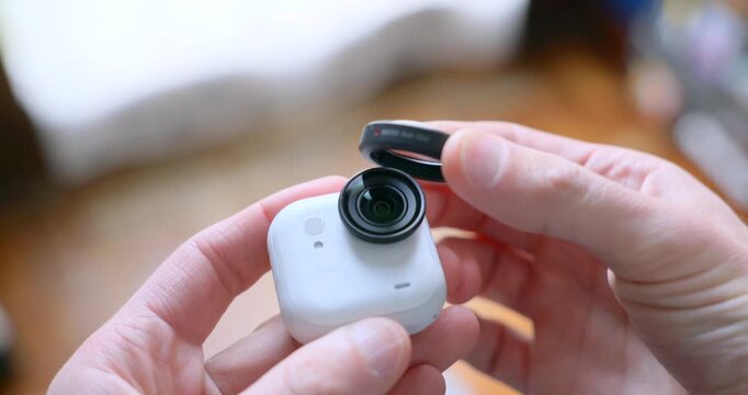 Close-up of hands attaching magnetic ND filter to lens of small white action camera like Insta360 Go