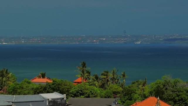 Close up drone shot of Bali&rsquo;s lush tropical coast and turquoise ocean; Bukit Peninsula and Garuda Wisnu Kencana Statue landmark visible on the horizon, Uluwatu