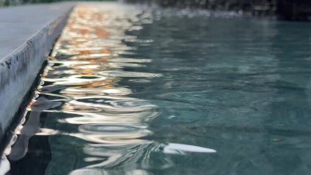 Gentle waves move across a calm water surface reflecting bright sunlight and creating shimmering highlights that drift across the frame. Sunlight reflections, water texture.