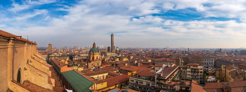 Aerial view of the medieval historic center with its iconic red rooftops, the Two Towers, and the dome of Santa Maria della Vita under a cloudy sky Bologna, Emilia-Romagna, Italy.