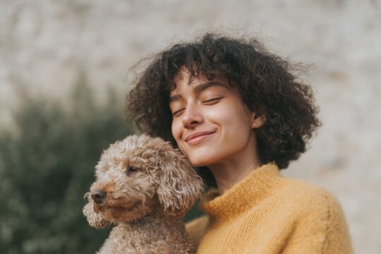 A woman with a warm smile on her face holding a small brown dog in her arms. the background is slightly blurred giving the focus to the woman and her pet.