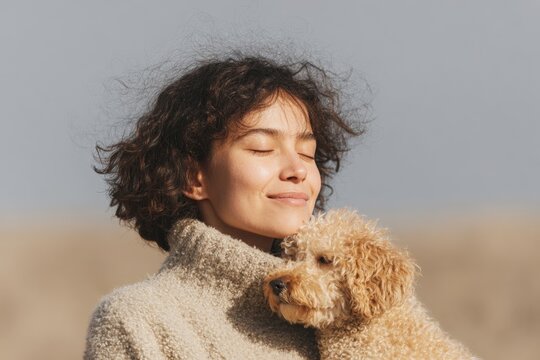 A woman wearing a creamcolored dress holding a brown dog in her arms with a blurred background.