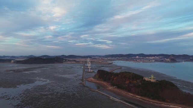 Drone flying over Nue Island Lighthouse Observatory showing Tando Port Sea Road and wind turbines standing on vast tidal flats under blue hour sky in South Korea
