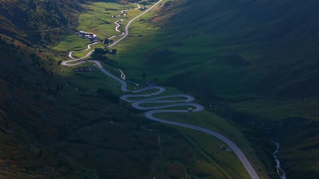 Serpentine road with hairpin turns snaking through green alpine valley in Julier Pass, Switzerland. Aerial drone panoramic view, spin shot