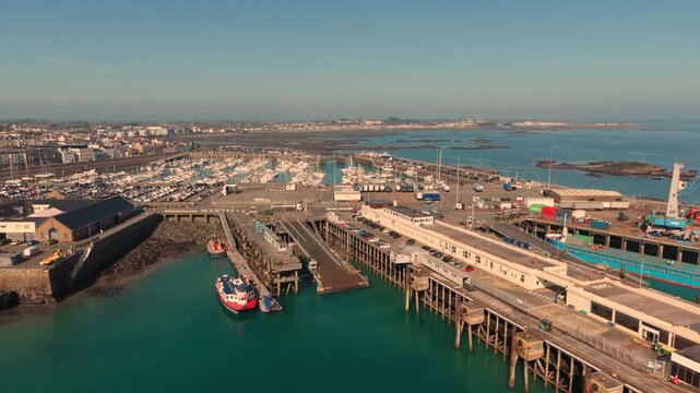St Peter Port Harbour Guernsey.Reveal of the ferry berth and docks with the rocky outcrops of Belle Greve Bay and QEII Marina in the background and ship in port in late afternoon sun