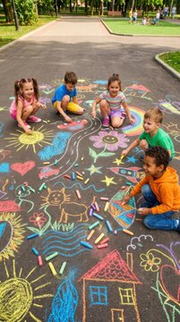 Group of children drawing with colorful chalk on pavement in park. Kids playing together outdoor on sunny day. International Childrens Day celebration and creative school vacation activity.