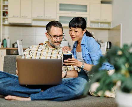 Portrait of a lovely young couple using a laptop and a mobile phone  together and having fun sitting on sofa at home