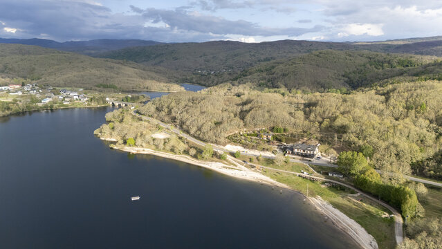 Aerial view of Encoro de Prada reservoir surrounded by lush forested hills and a small village under a cloudy sky A Veiga, Ourense, Spain.